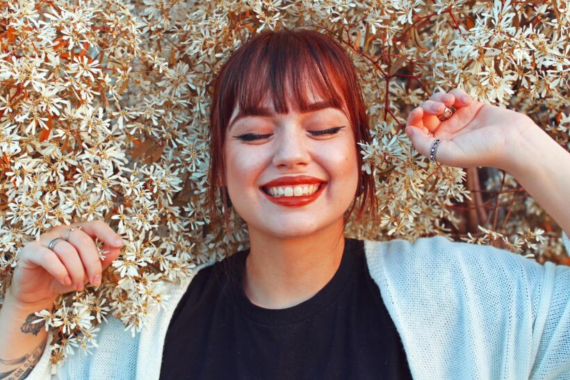 Redhead woman smiling with closed eyes, surrounded by blooming flowers, radiating joy and happiness.