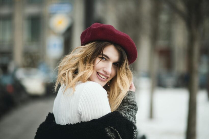 A joyful woman in winter attire with a burgundy beret, posing outdoors on a snowy day.