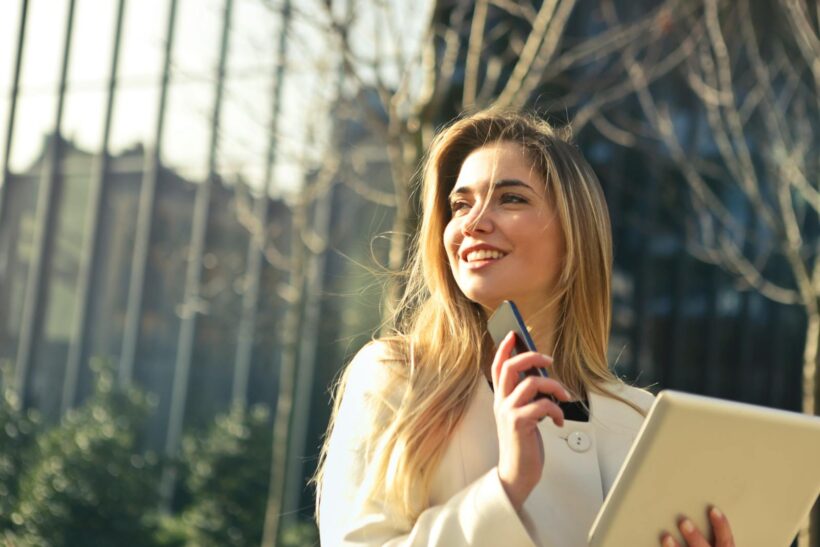 Smiling businesswoman holding smartphone and tablet outdoors in Milan.